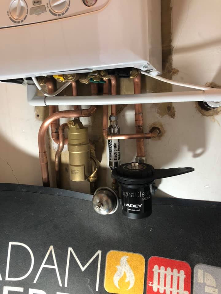 Copper pipework and connections beneath a boiler, with Adam’s protective work mat