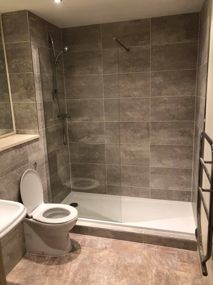 Finished grey-tiled bathroom with a glass screen, toilet and towel radiator